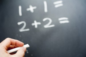 Closeup of a teacher writing simple sums in chalk on a blackboard
